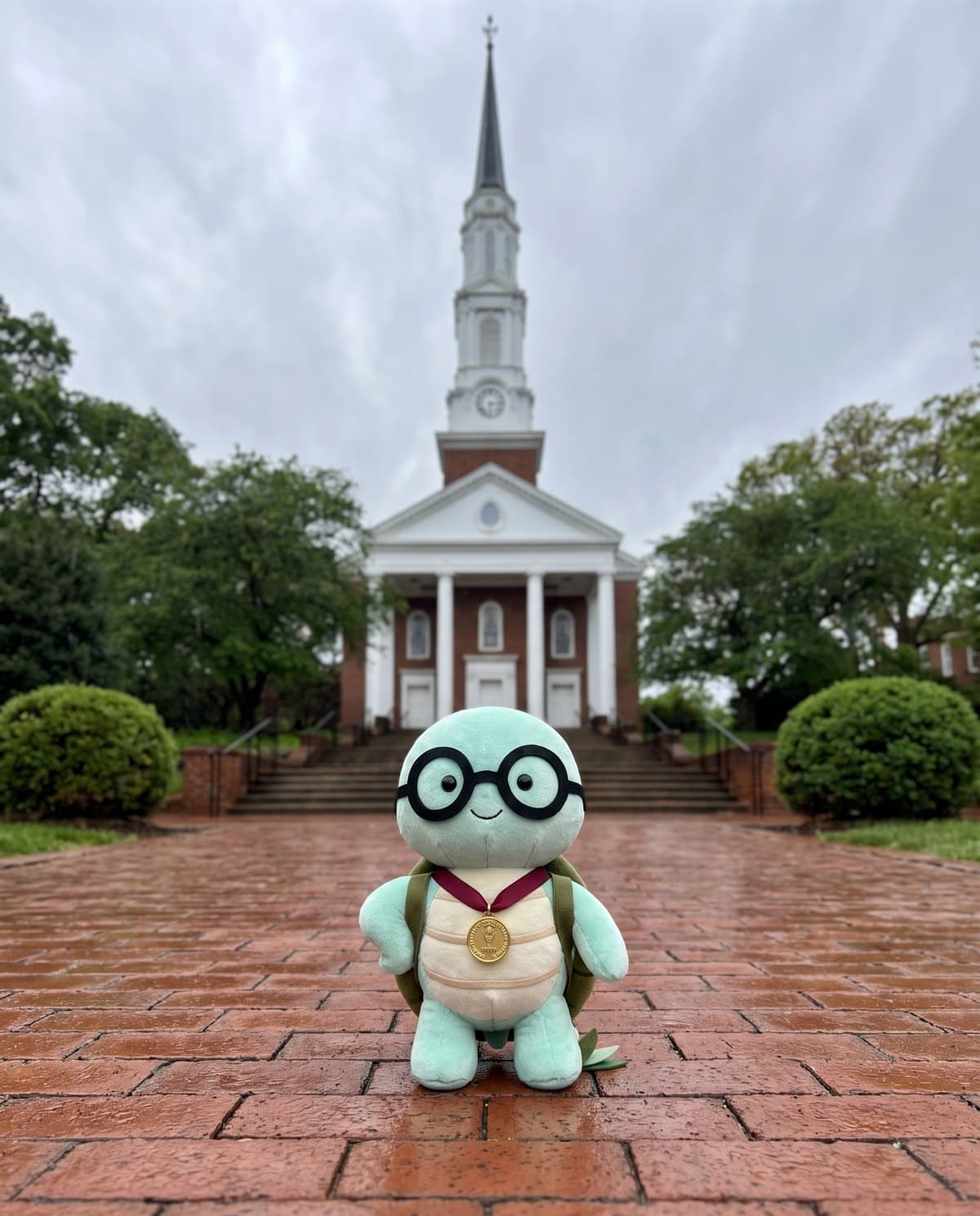 The NoTestudo plush wearing a gold medal on the wet brick path in front of Memorial Chapel on an overcast day