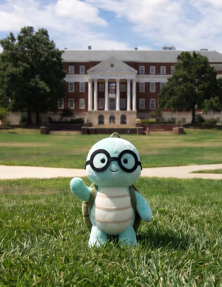 The NoTestudo plush waving on the lawn of McKeldin Mall, McKeldin Library behind it.